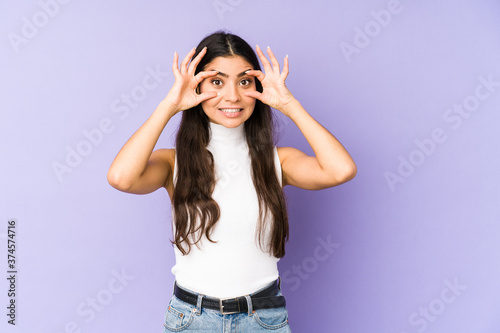 Young indian woman isolated on purple background keeping eyes opened to find a success opportunity.