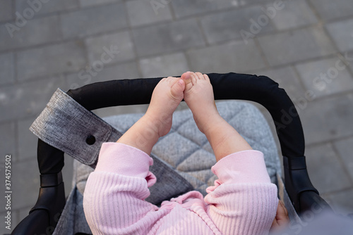 in  gray baby carriage,  small legs of  newborn are visible, child in pink camps, concept of walking on  street