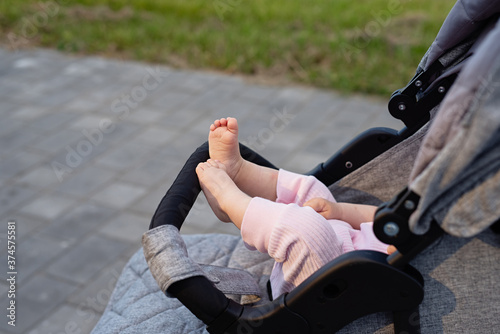 in gray baby carriage, small legs of newborn are visible, child in pink camps, concept of walking on street