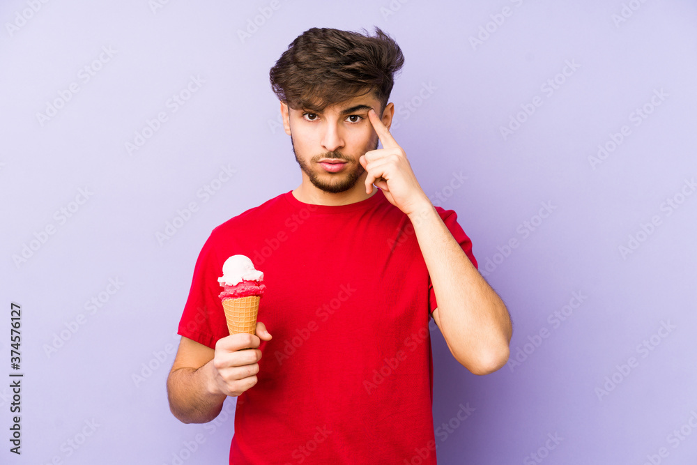 Young arabian man holding a ice cream pointing temple with finger, thinking, focused on a task.