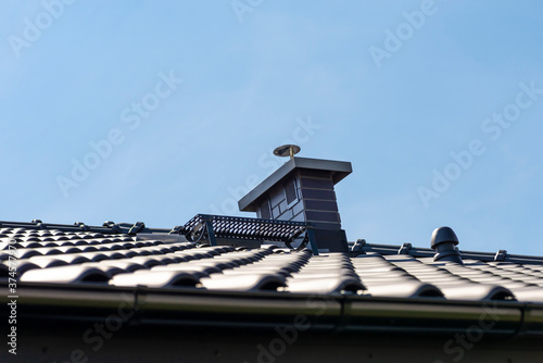 The roof of a single-family house covered with a new ceramic tile in anthracite against the blue sky. Vsible system chimney covered with tiles. photo