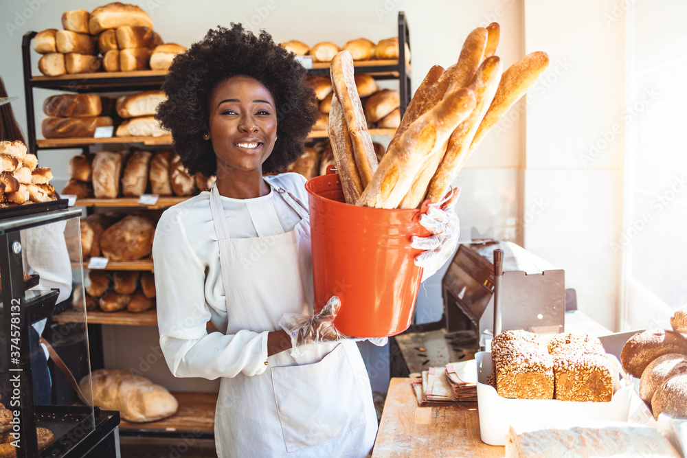 Cheerful female baker is standing and holding a basket of pastry. She