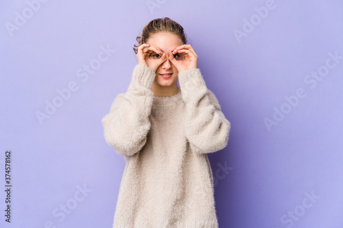 Young caucasian woman on purple background showing okay sign over eyes