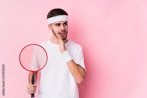 Young caucasian man playing badminton isolated is saying a secret hot braking news and looking aside © Asier