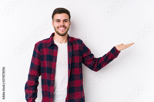 Young caucasian man posing in a white background isolated showing a copy space on a palm and holding another hand on waist.