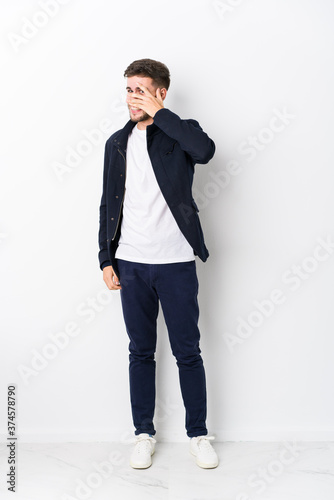 Full body young caucasian man isolated blink at the camera through fingers, embarrassed covering face.