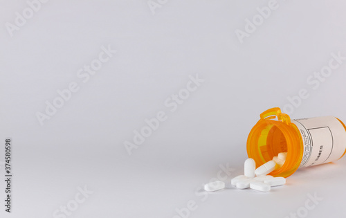 pill bottle lying on its side with white tablet pills spilling out on a white background with copy space in landscape format