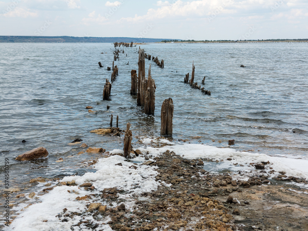 Salty estuary Kuyalnik, dead lake near Odessa, Ukraine. Wooden sticks reflected in blue water at sunny weather. Salty estuary Kuyalnik, dead lake near Odessa, Ukraine. Wooden sticks reflected in blue water at sunny weather.