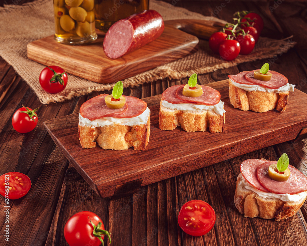 Delicious canapes with salami, cream cheese, olives and tomatos on a wooden background