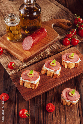 Delicious canapes with salami, cream cheese, olives and tomatos on a wooden background