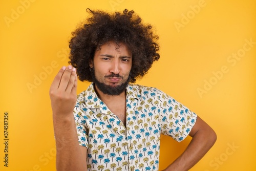 Young man with afro hair over wearing hawaiian shirt standing over yellow background angry gesturing typical italian gesture with hand, looking to camera © Roquillo