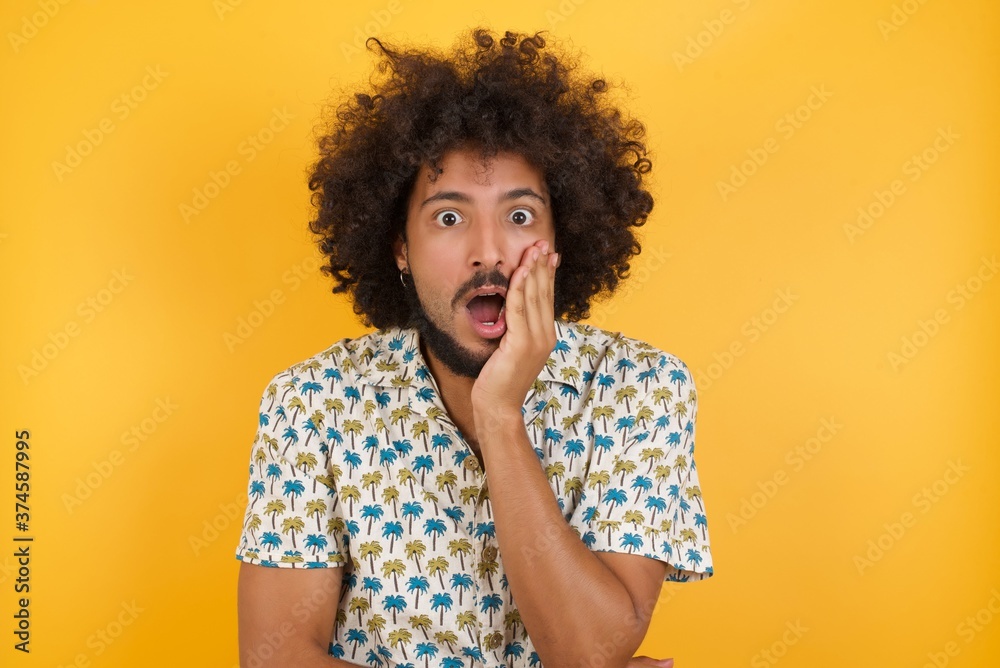 Horizontal portrait of shocked Young man with afro hair wearing hawaiian shirt standing looks with great surprisment being very stunned, astonished with unexpected news, . Facial expressions concept. Horizontal portrait of shocked Young man with afro hair wearing hawaiian shirt standing looks with great surprisment being very stunned, astonished with unexpected news, . Facial expressions concept.