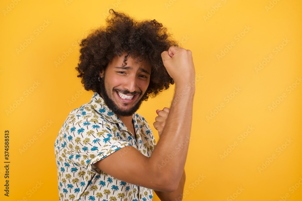 Profile photo of excited Young man with afro hair over wearing hawaiian shirt standing over yellow background raising fists celebrating black friday shopping Profile photo of excited Young man with afro hair over wearing hawaiian shirt standing over yellow background raising fists celebrating black friday shopping