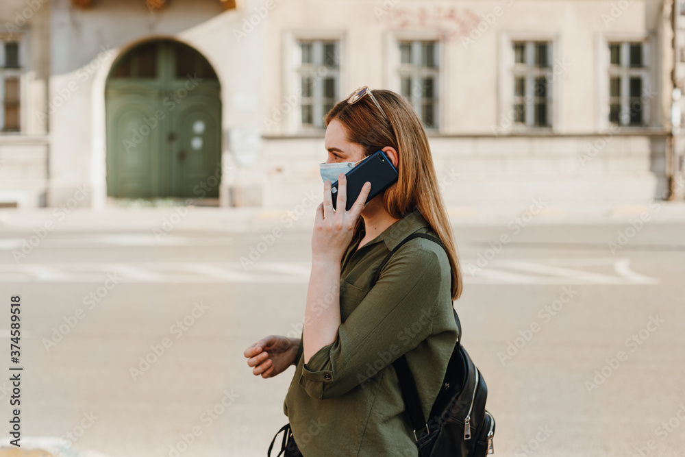 Woman with face mask talking on the phone outside, profile view