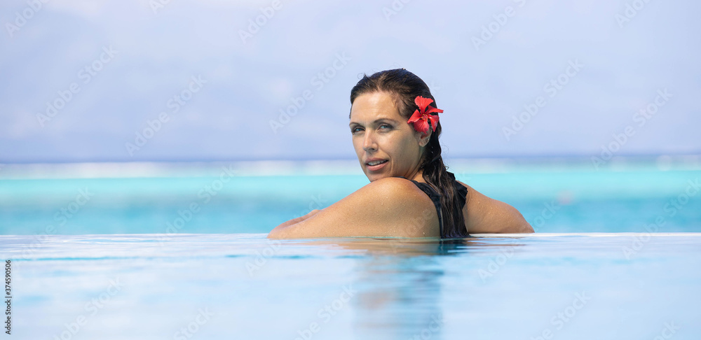 Beautiful woman on vacation at a tropical island resort swimming in a blue infinity pool overlooking the ocean