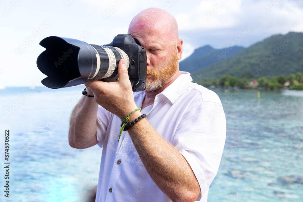 Obraz premium Professional photographer holds camera with long lens taking a picture on a tropical island