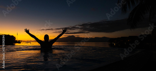 Silhouette man with arms raised in swimming pool during sunrise on a tropical island