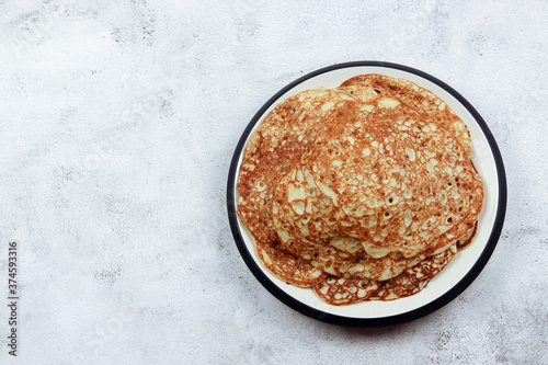 Traditional russian yeast pancakes on a round plate on a light gray background. Top view, flat lay