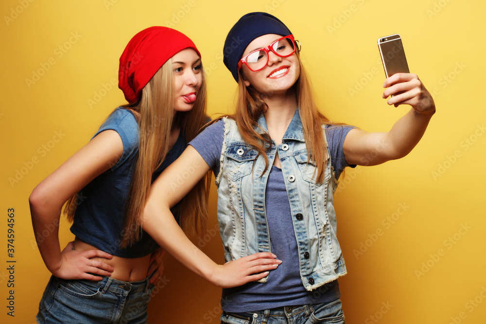 two young hipster girls friends taking selfie over yellow background two young hipster girls friends taking selfie over yellow background