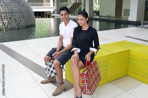 Asian young attractive man woman sitting on a bock bench with shopping bags