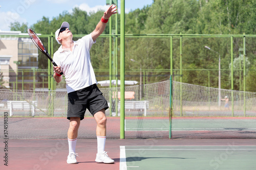 An elderly man plays tennis on an outdoor court © Дворецкая Таня