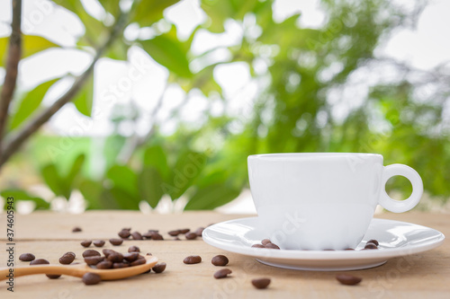 A white hot coffee cup with a saucer and spoon is placed on a wooden plate on the landscape nature background.