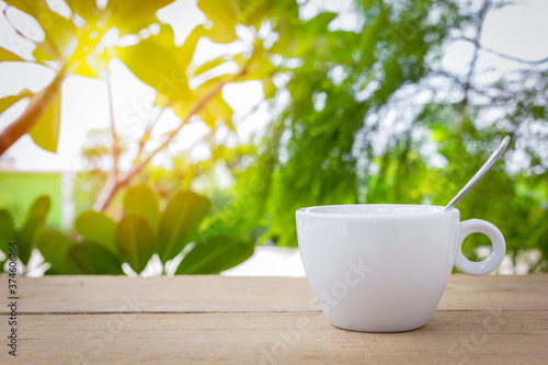 A white hot coffee cup with spoon is placed on a wooden plate and on the landscape nature background.