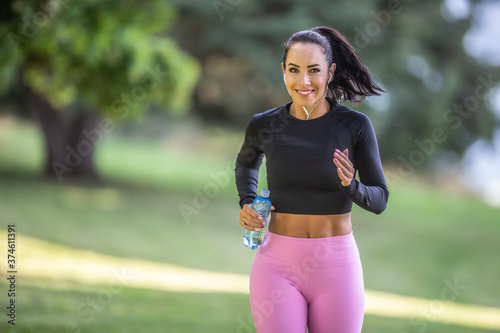 Fototapeta Naklejka Na Ścianę i Meble -  Attractive young woman running in the park with bottle of water