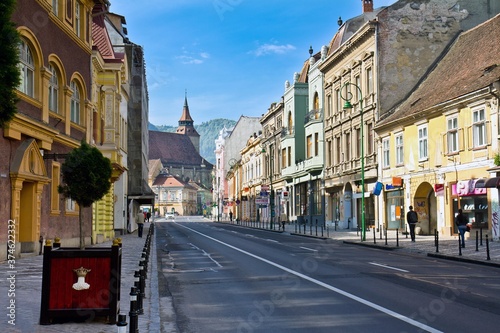 BRASOV, ROMANIA - APRIL 23, 2016. Street full of shops and small european houses and the Black Church in the background in a sunny day in Brasov, Romania.