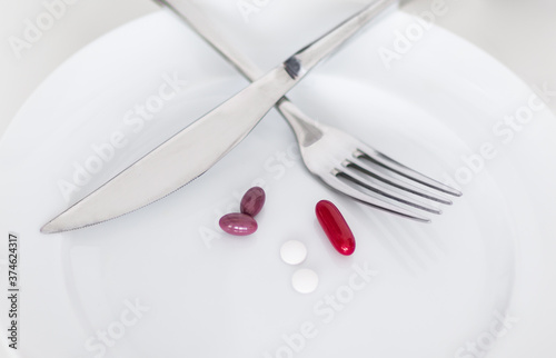 Diet tablets and medicine pills served as a meal to eat on a plate with cutlery. 