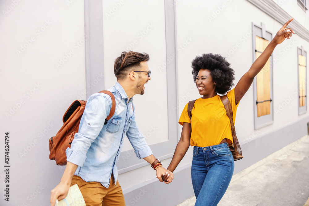 Young cheerful overjoyed couple walking on the street and having fun. Man holding a map. Tourism concept.