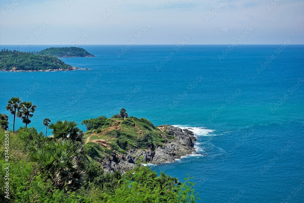 Tropical green islands on the turquoise surface of the Andaman Sea. Palm trees on a background of water. On the rocky coast, the foam of the waves. Azure clear sky. Summer day. Thailand. Phuket.