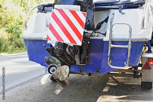 Motor boat transom close-up on car trailer with large size load cargo sign on outboard motor lower unit with stainless sieel propeller on road at Sunny summer day, motor boats safety transportation photo