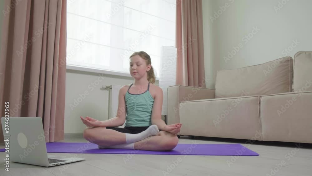The girl practices yoga at home and performs the lotus position. Online physical exercise training. Sports at home. Athletic body. Slimming exercises. Sports and recreation concept. The girl practices yoga at home and performs the lotus position. Online physical exercise training. Sports at home. Athletic body. Slimming exercises. Sports and recreation concept.