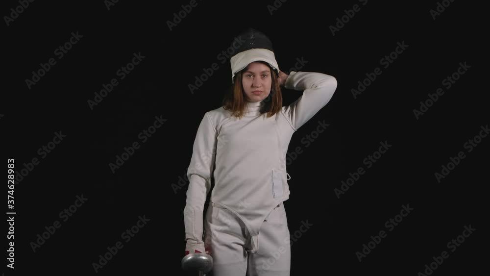 Portrait of a professional woman fencing athlete which puts on a protective mask and becomes in a fighting pose holding a sword. Black background. Slow motion. Close up. Portrait of a professional woman fencing athlete which puts on a protective mask and becomes in a fighting pose holding a sword. Black background. Slow motion. Close up.