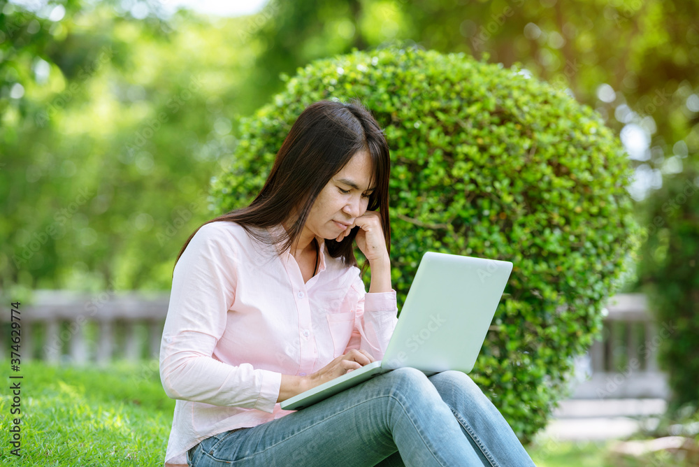 Asian woman sitting green park using laptop computer. Woman working on laptop happy entrepreneur business using notebook with hands typing on keyboard home office during coronavirus quarantine period Asian woman sitting green park using laptop computer. Woman working on laptop happy entrepreneur business using notebook with hands typing on keyboard home office during coronavirus quarantine period