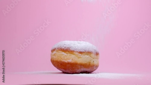 Appetizing donut with a lot of powdered sugar on top. A very sweet dessert. Pink background.
