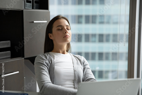 Sleepy tired businesswoman with closed eyes sitting at desk in modern office, meditating, taking break, exhausted overworked young woman employee student resting, napping, stress relief concept photo