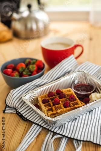 Belgian waffles for breakfast. Waffles with fresh berries and berry jam. Cup of coffee and teapot on the table. Breakfast in the trailer
