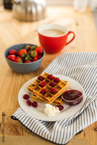 Belgian waffles for breakfast. Waffles with fresh berries and berry jam. Cup of coffee and teapot on the table. Breakfast in the trailer