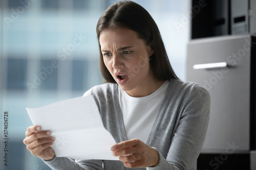 Angry annoyed young businesswoman employee reading letter, working with correspondence, frustrated stressed woman received bad news, holding document, dismissal or debt notification photo