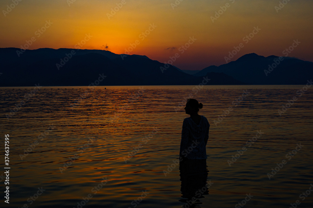 silhouette of a girl on the background of sea mountains and sunset