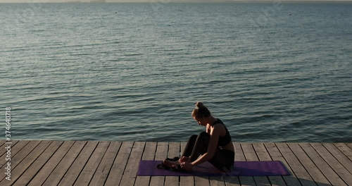 Wallpaper Mural Outdoors sport concept. Woman is putting socks on her feet sitting on sport mat on river pier at summer, side view. Young female in black top and leggings preparing to physical exercises. Torontodigital.ca