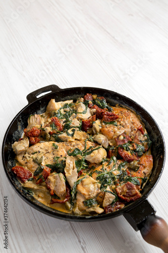 Homemade Creamy Tuscan Chicken in a cast-iron pan on a white wooden background, low angle view. Copy space.