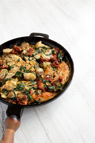 Homemade Creamy Tuscan Chicken in a cast-iron pan on a white wooden background, low angle view. Space for text.