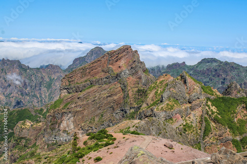 Una gran montañas de rocas con pasto verde en lo mas alto de las nubes blancas y un cielo azul  photo