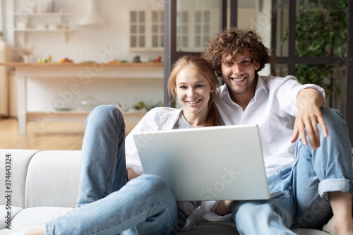 Happy couple using laptop while sitting on couch.