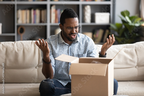 Принти на полотні Angry irritated African American man in glasses dissatisfied by received parcel,