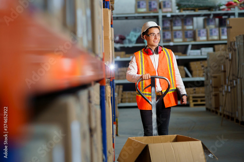 Male logist in the warehouse stands with a pallet loader and unloading goods photo