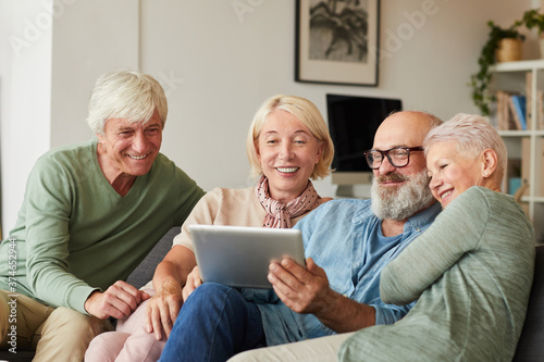 Group of senior people sitting on sofa and watching something on digital tablet at home